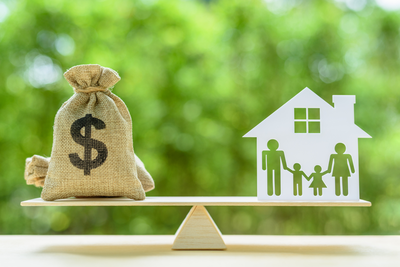 balance with sack of money on one side and model of family in a house on the other