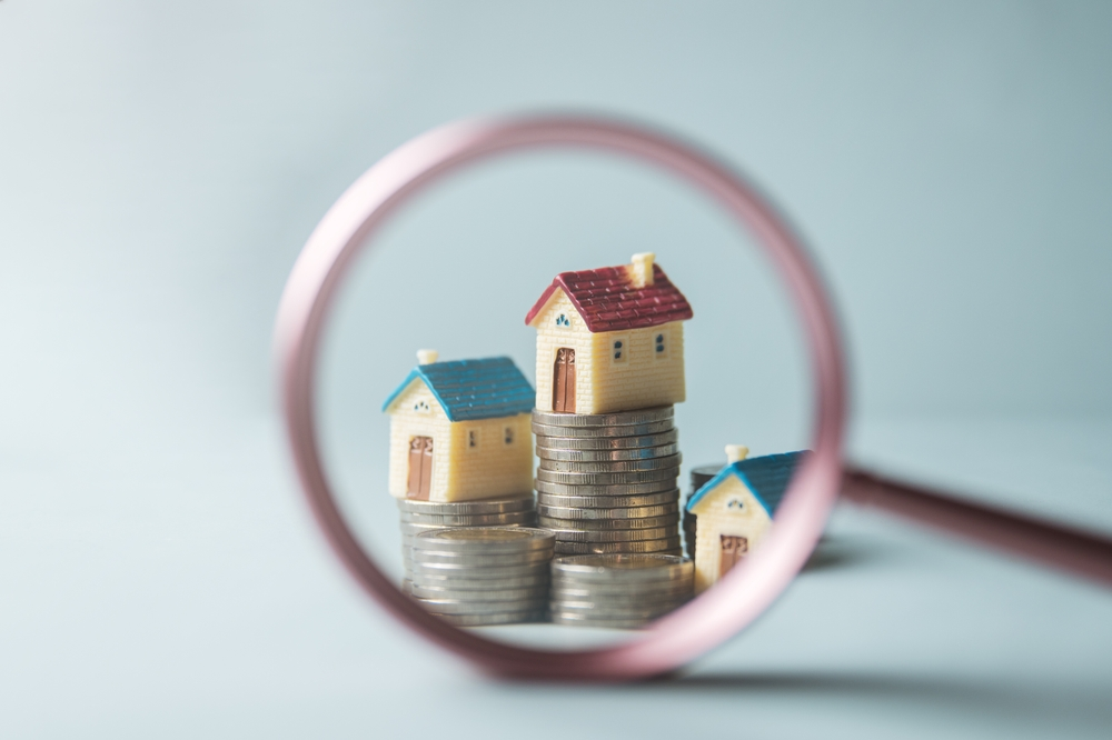 magnifying glass over models of homes on stacks of coins